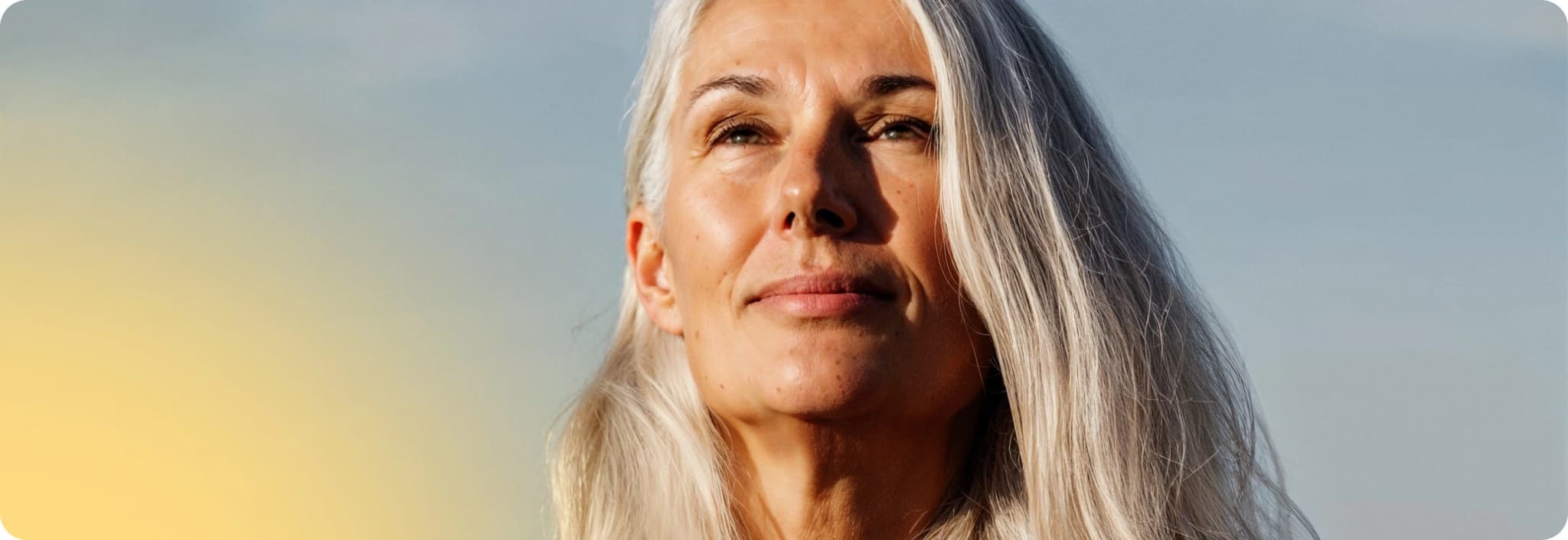 A person with long grey hair against a soft gradient sky background.